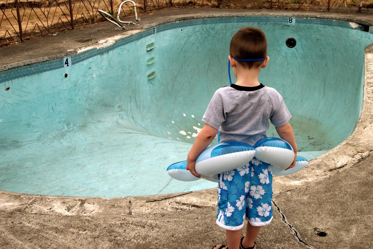 Kleiner Junge mit Schwimmreifen steht vor einem ausgelassenen, alten Swimmingpool